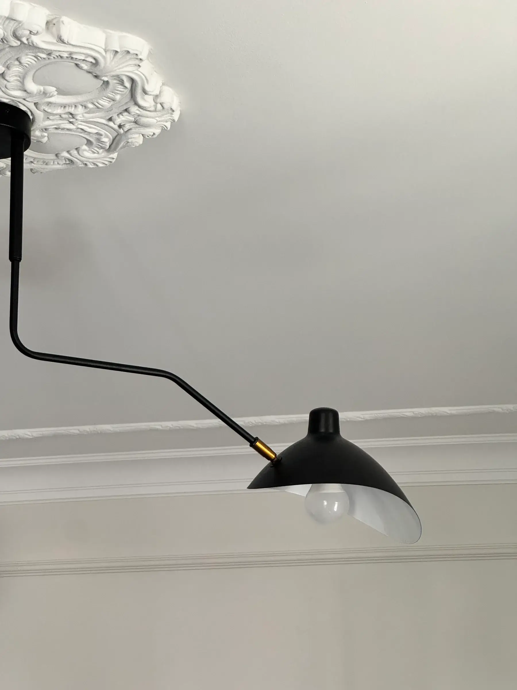 Czarna lampa z ruchomym ramieniem pod sztukateryjną rozetą
